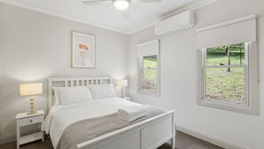 A bedroom with a bed, bedside tables, a lamp, a framed picture, an air conditioning unit, and a window with a view of a garden. - WOODBINE LODGE- Picture perfect and meticulously maintained (Marysville)
