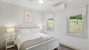 A bedroom with a bed, bedside tables, a lamp, a framed picture, an air conditioning unit, and a window with a view of a garden. - WOODBINE LODGE- Picture perfect and meticulously maintained (Marysville)