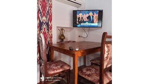 Un comedor con una mesa de madera y cuatro sillas, un televisor de pantalla plana montado en la pared y un equipo de aire acondicionado.