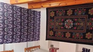 Una habitación con dos camas de madera, un tapiz estampado y un adorno colgante en la pared.