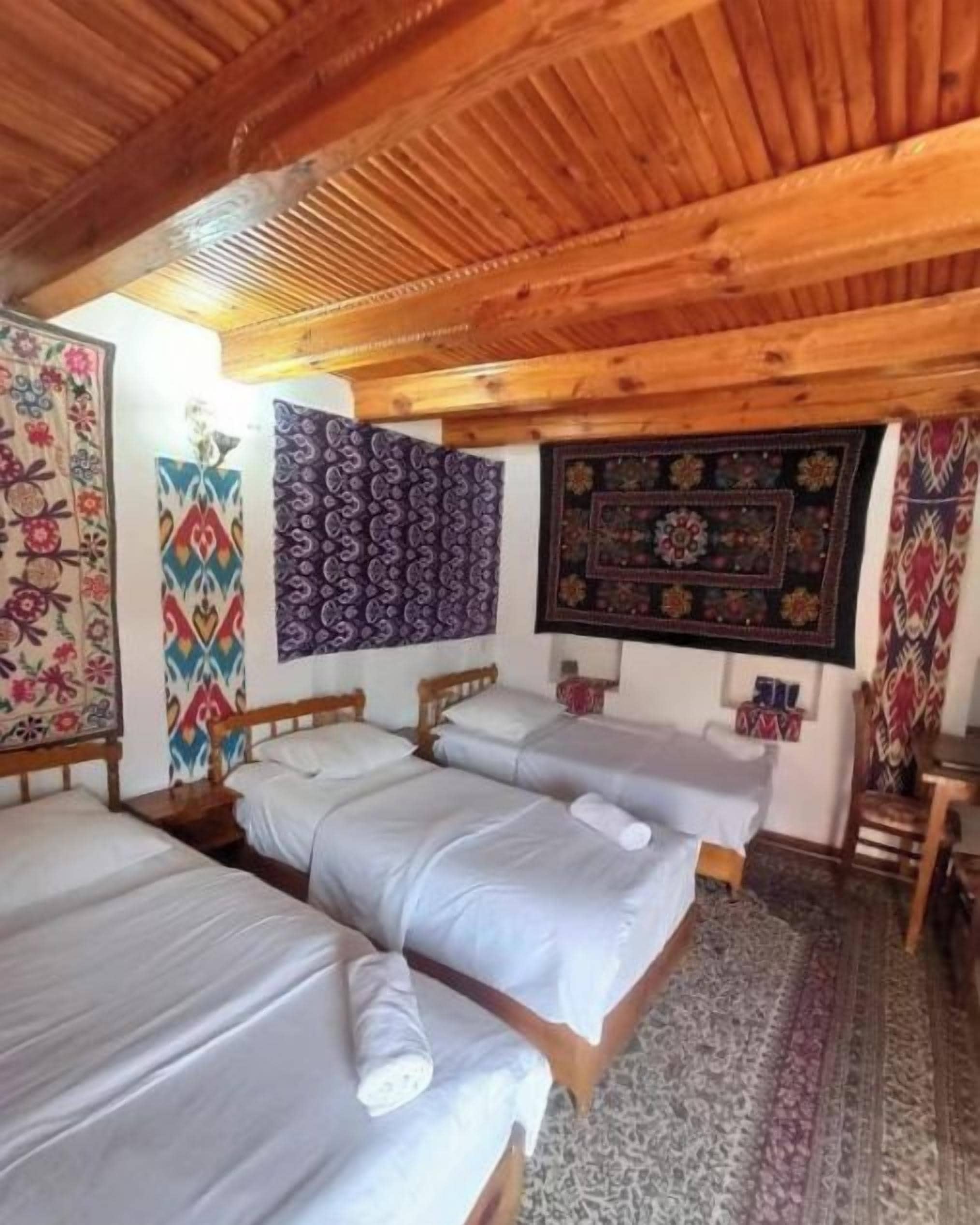 A room with three beds, wooden ceiling beams, and patterned wall hangings.