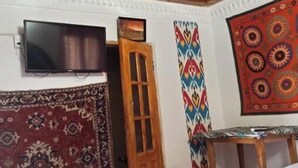 Una habitación con techo de madera, un televisor en la pared, un tapete estampado, un tapiz de colores y una pequeña mesa.