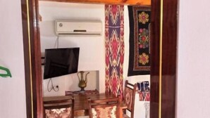 Una habitación con techo de madera, televisor montado en la pared, una mesa con sillas y una alfombra estampada.