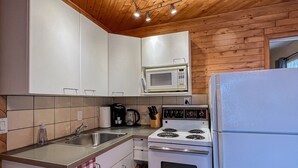 A kitchen with wooden ceiling, white cabinets, a microwave, stove, and refrigerator. - Ahmic Lake Resort's 1-Bedroom Cottage w/ hot tub (LOON Cottage) (Magnetawan)