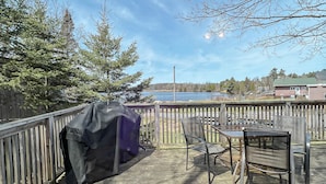 A wooden deck with a covered grill, a table, and chairs. - Ahmic Lake Resort's 1-Bedroom Cottage w/ hot tub (LOON Cottage) (Magnetawan)