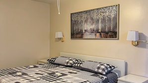 A bedroom with a bed, a ceiling fan, a nightstand, a lamp, and a painting on the wall. - Ahmic Lake Resort's 1-Bedroom Cottage w/ hot tub (LOON Cottage) (Magnetawan)