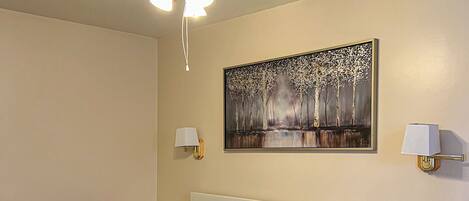 Une chambre à coucher avec un lit, un ventilateur de plafond, une table de chevet, une lampe et un tableau au mur.