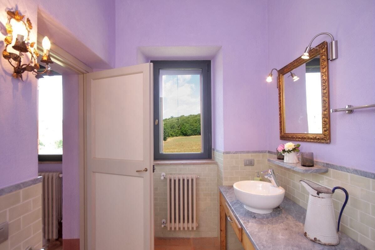 A bathroom with a window, a sink, a mirror, and a radiator.
