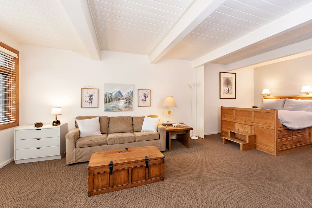 Una habitación acogedora con una cama de madera, un sofá color beige, un aparador de madera y una mesita de noche con una lámpara.