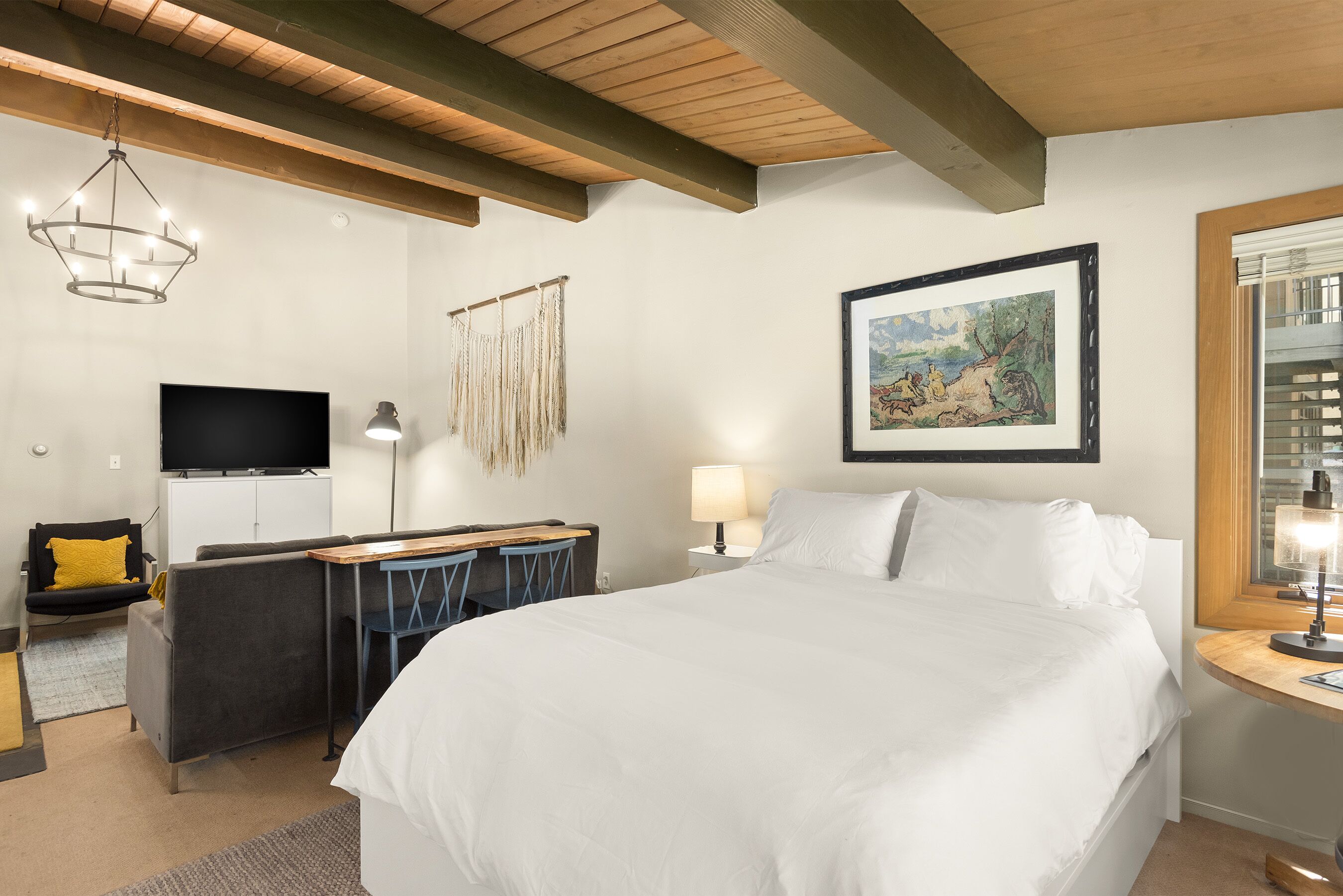 Une chambre d’hôtel avec un grand lit, un bureau avec une chaise, une télévision, une lampe et un tableau encadré au mur.