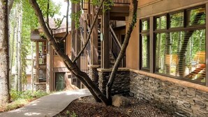 A building with a stone facade, large windows, and a tree in the foreground. - Aspenwood by Snowmass Vacations (Snowmass Village)
