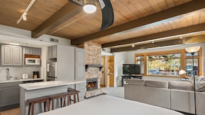 A modern kitchen with grey cabinets, a central island, and a stone fireplace. - Aspenwood by Snowmass Vacations (Snowmass Village)