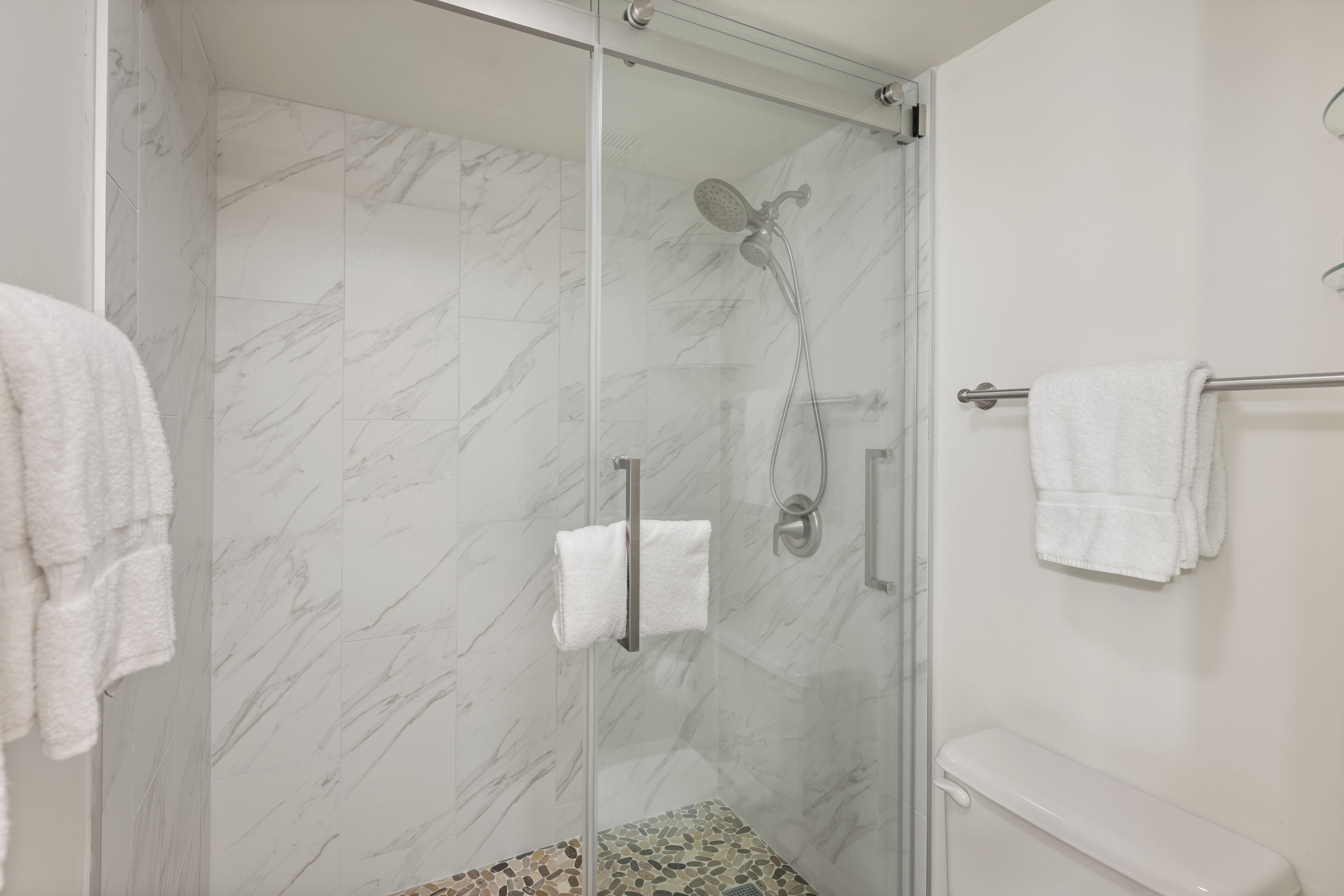 A modern bathroom with a glass-enclosed shower, marble walls, and a toilet with a towel rack.