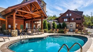 A wooden cabin with a pool, outdoor seating, and a stone pillar.