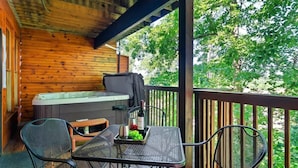 A wooden cabin with a hot tub, a table with chairs, and a view of trees.