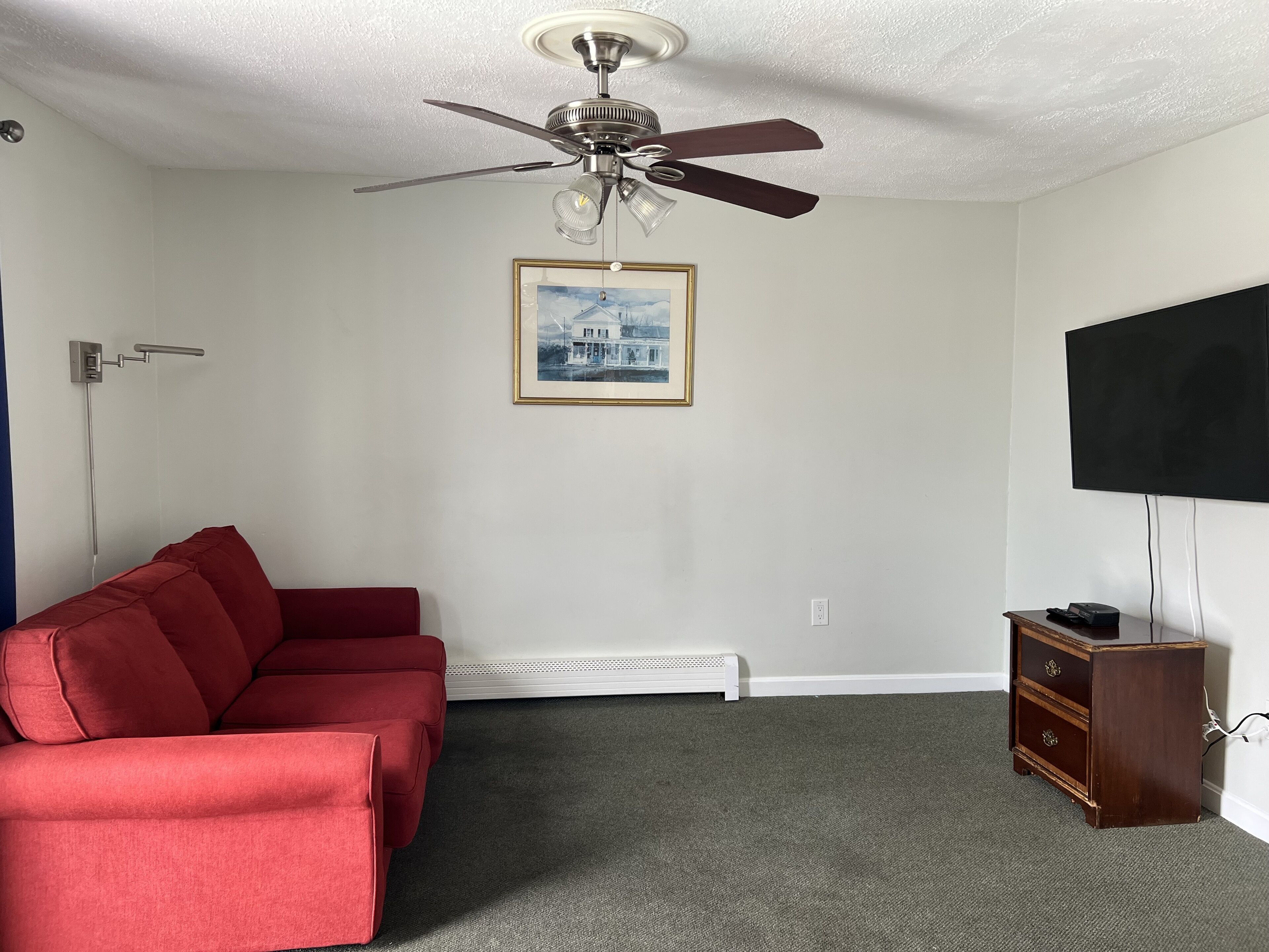 A room with a ceiling fan, a framed picture, a red sofa, a TV, and a wooden cabinet.