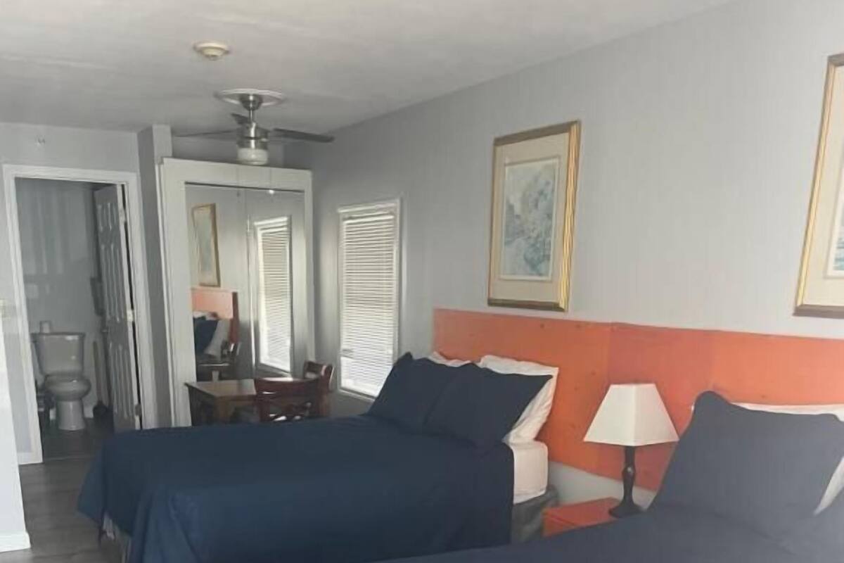 A hotel room with two beds, a desk, a chair, and a bathroom visible through an open door.