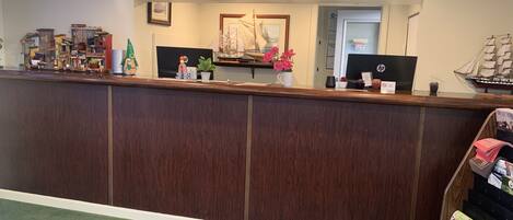 A reception desk with a wooden finish, a 'BIENVENIDO WELCOME ACCUEIL' sign above, and various decorative items including a model ship, flowers, and a small Christmas tree.