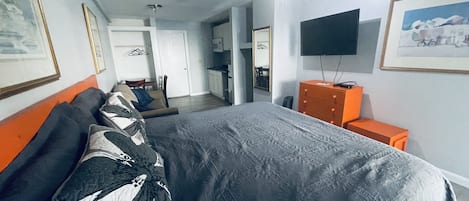 A hotel room with a large bed, a TV on the wall, and a kitchenette in the background.
