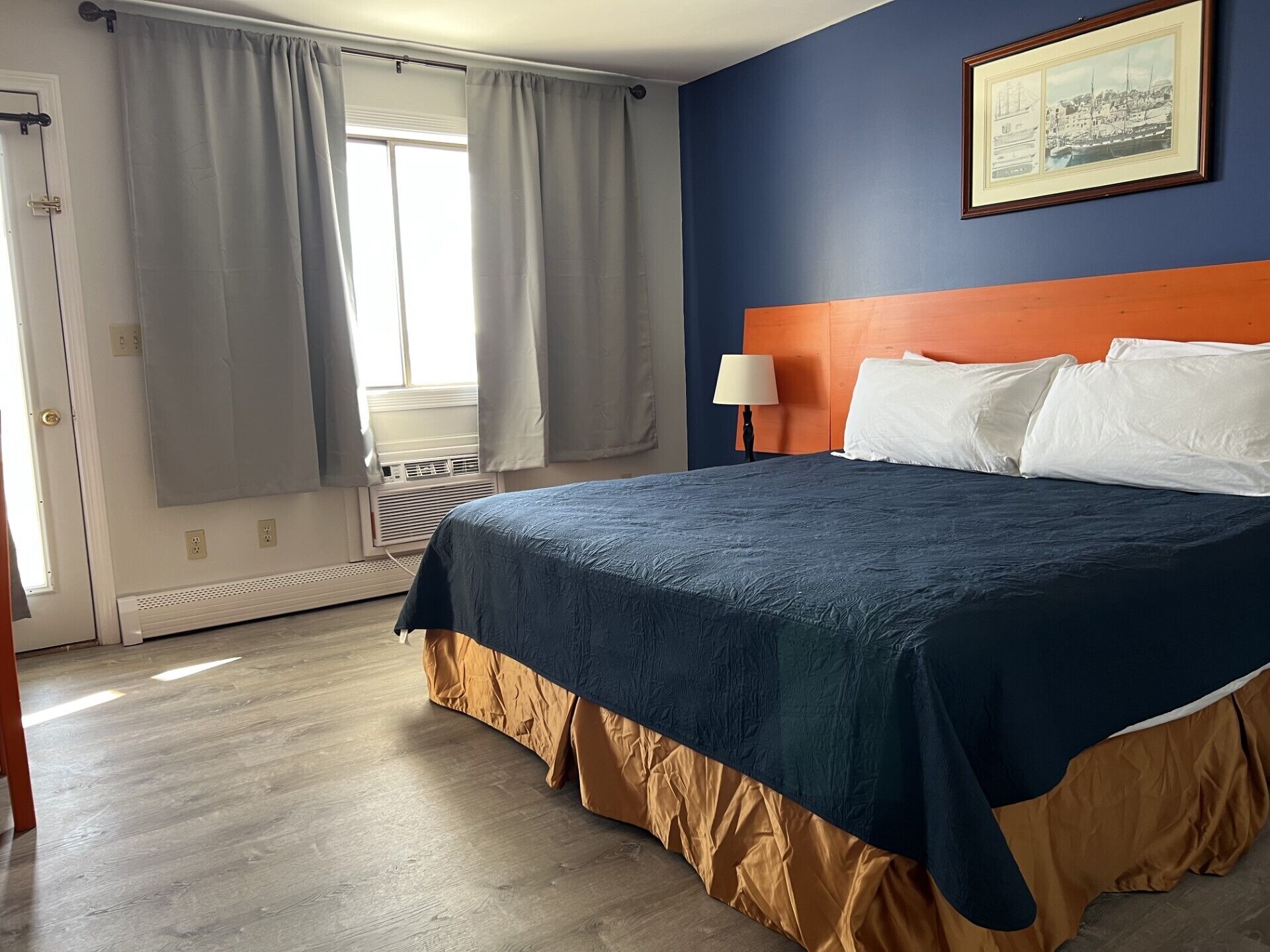 Habitación de hotel con una cama grande, un cabecero, una mesita de noche con lámpara y una ventana con cortinas.
