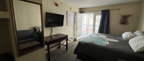 A hotel room with a bed, a desk with a TV, a chair, and a large mirror.