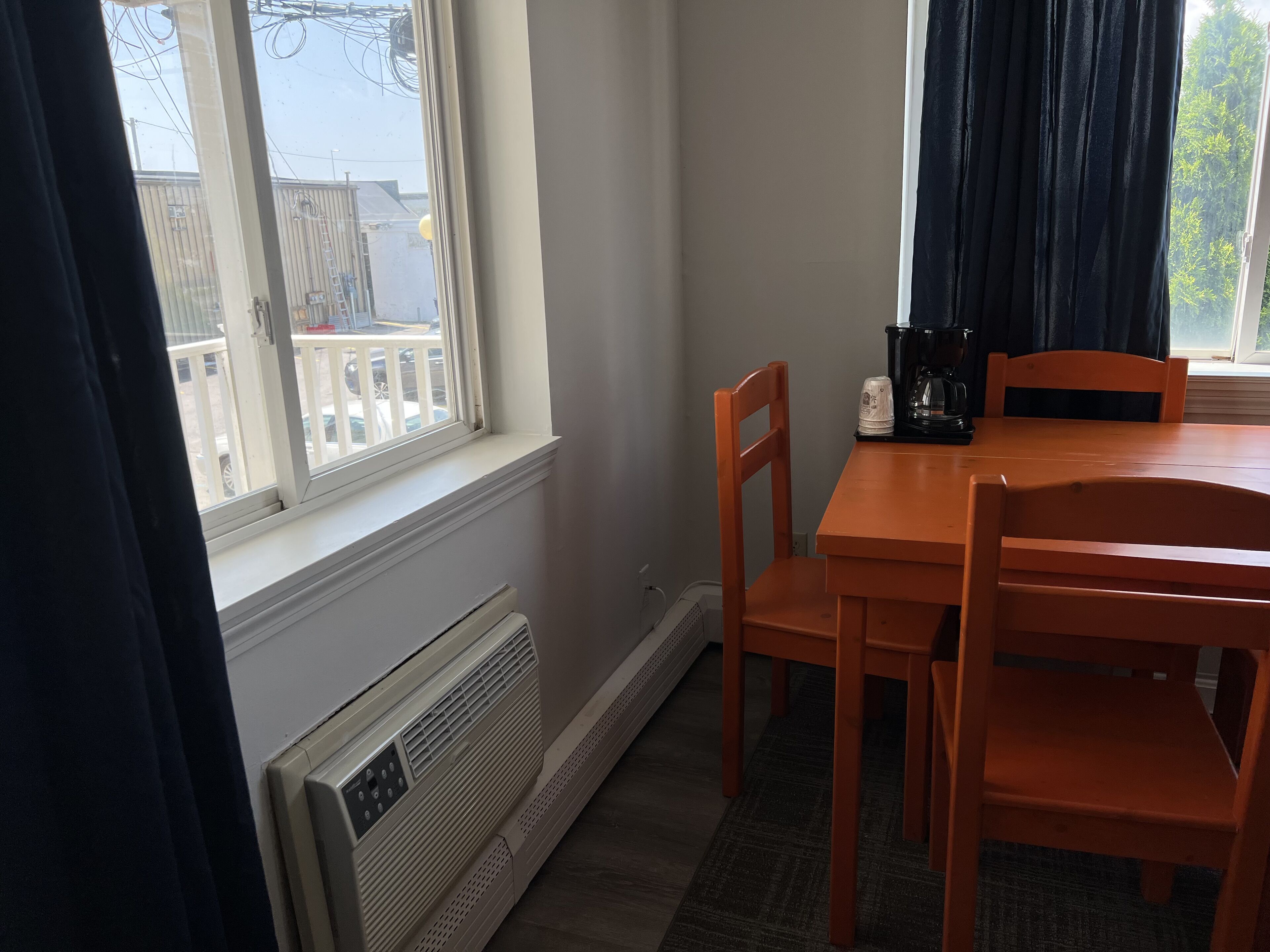 A dining area with a table and chairs, a window with a view of buildings, and a radiator.