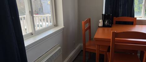 A dining area with a table and chairs, a window with a view of buildings, and a radiator.