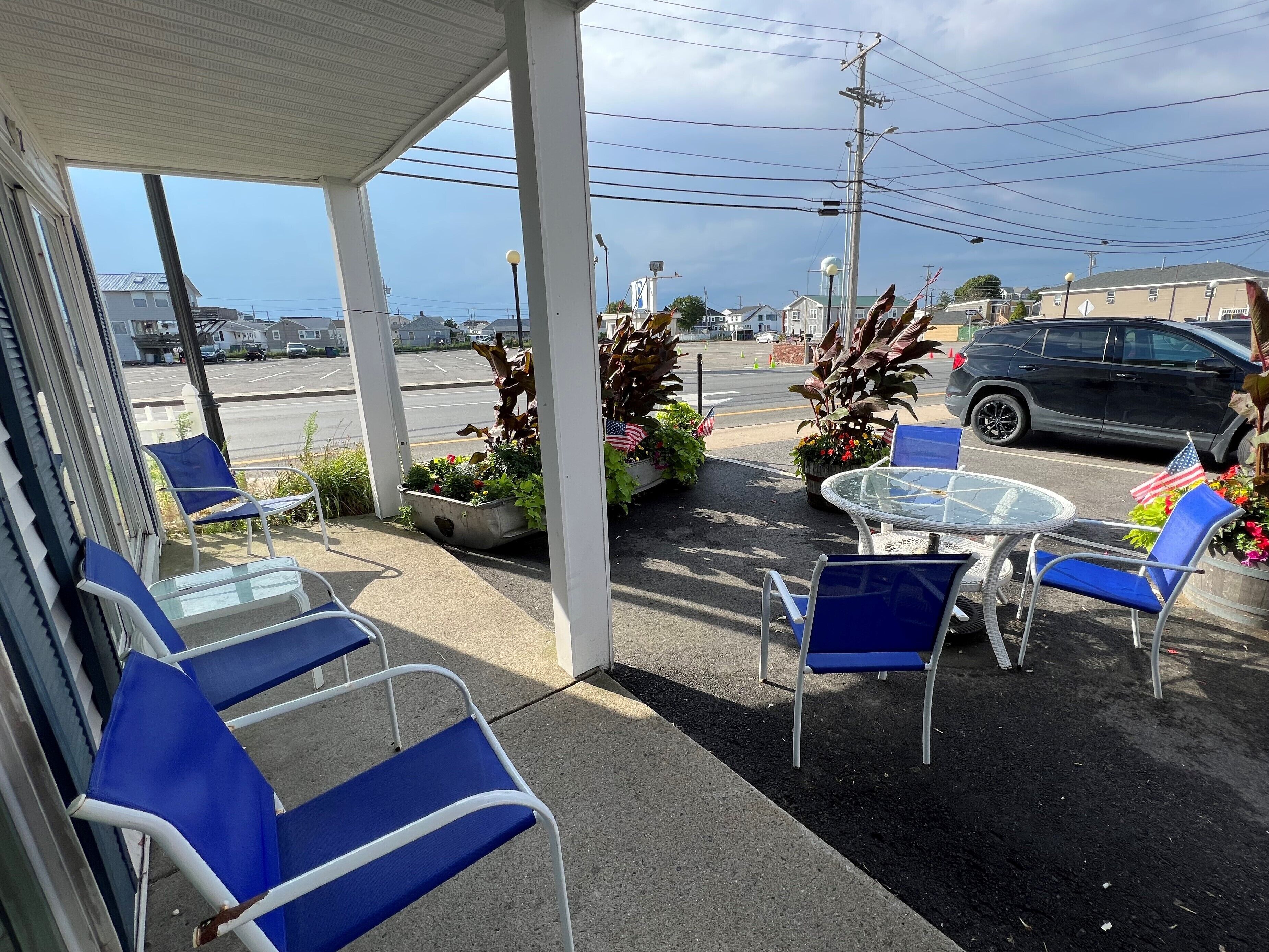 A covered outdoor seating area with blue chairs and a glass table, featuring potted plants and American flags.