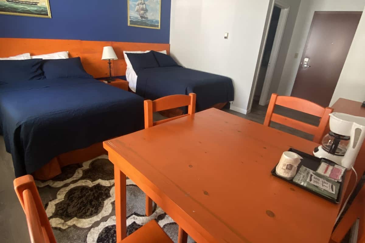 A hotel room with two beds, a wooden table, and orange chairs.