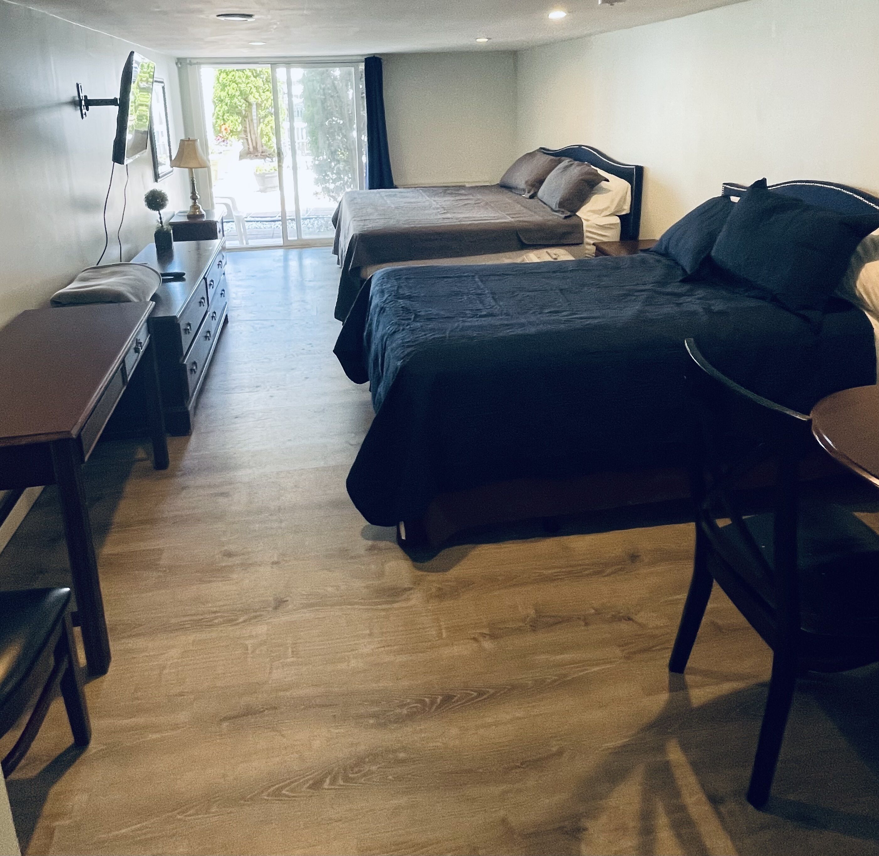 A hotel room with two beds, a desk, a chair, a lamp, and a TV.