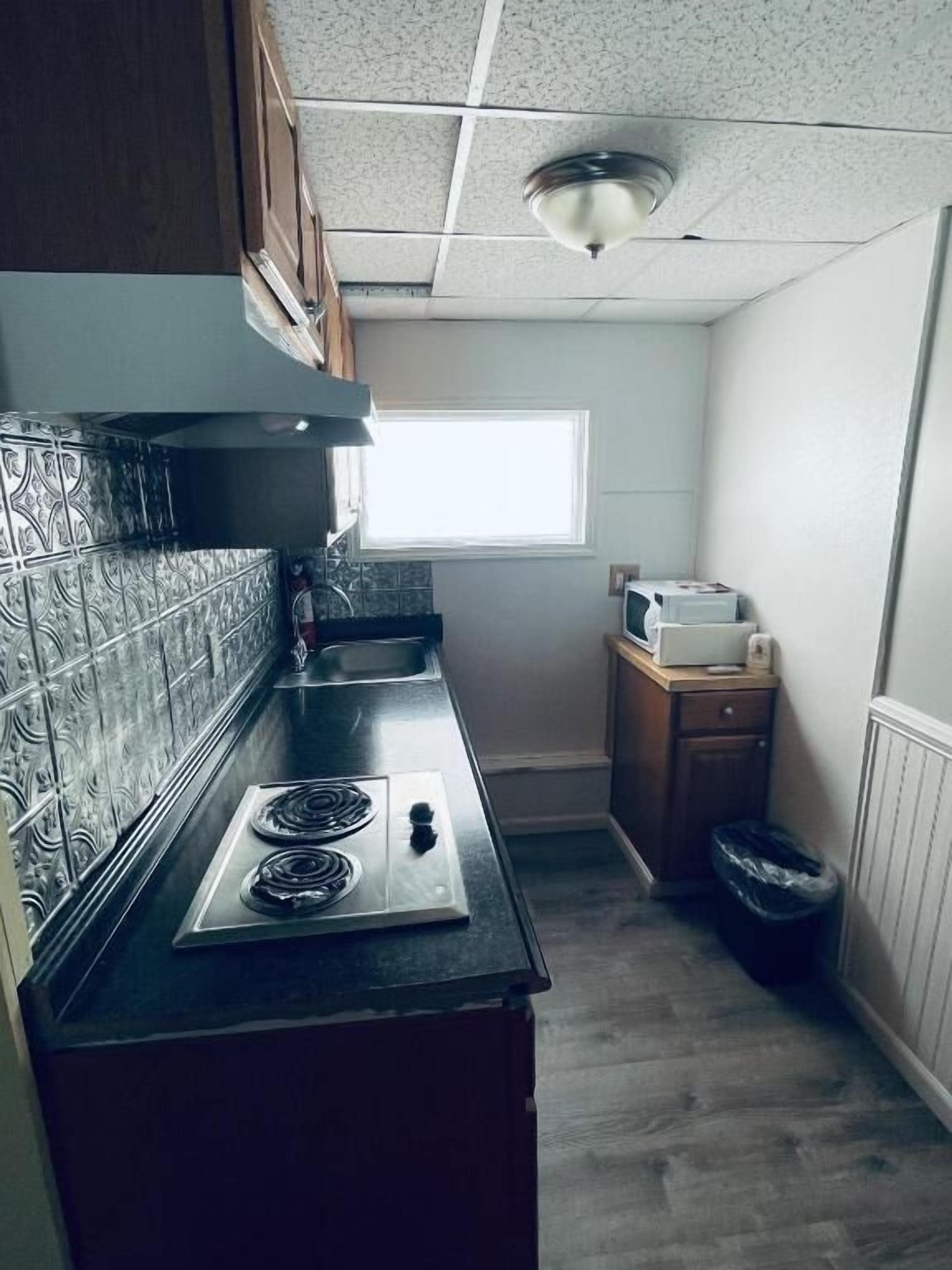 Une cuisine compacte équipée d’une cuisinière à gaz, d’un four à micro-ondes et d’une fenêtre laissant entrer la lumière naturelle.