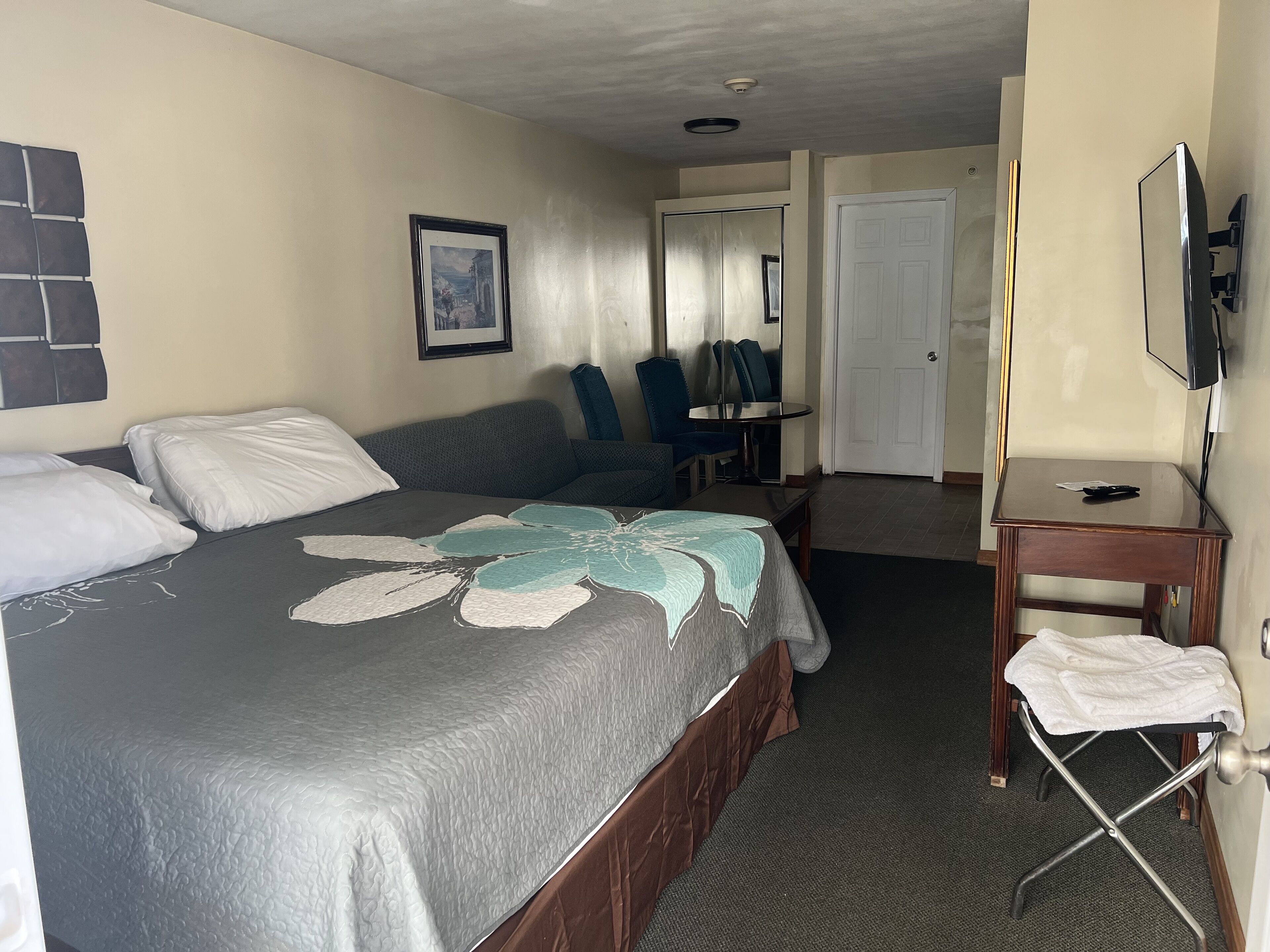 Une chambre d’hôtel avec un lit, un bureau, une chaise, une télévision et une porte.