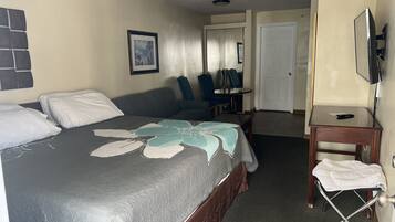 Une chambre d’hôtel avec un lit, un bureau, une chaise, une télévision et une porte.