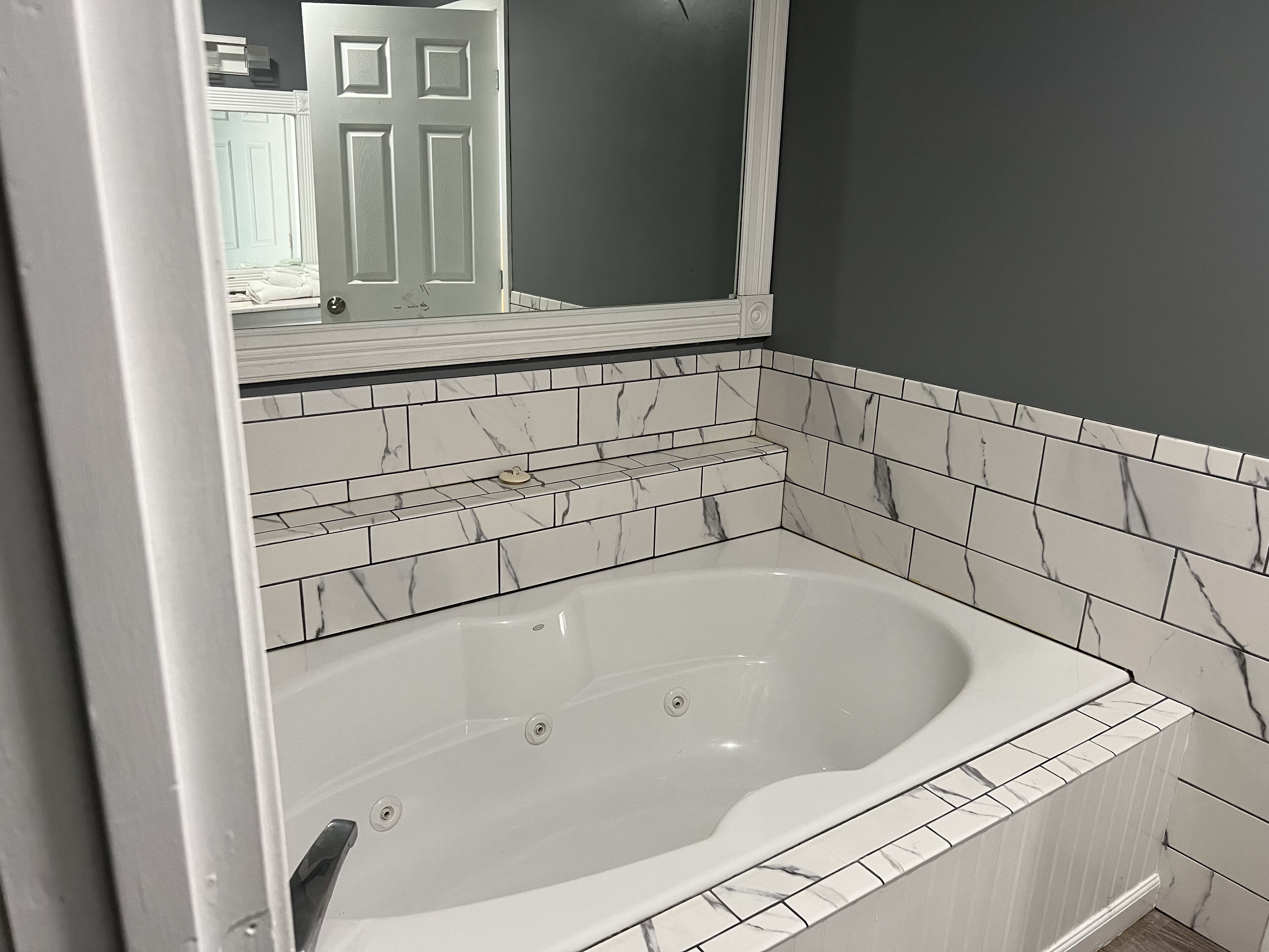 A bathroom with a white bathtub, marble-patterned tiles, and a large mirror above the tub.