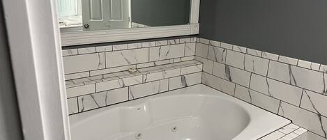 A bathroom with a white bathtub, marble-patterned tiles, and a large mirror above the tub.