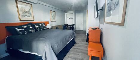 A hotel room with a bed, a desk, and a chair. There are framed pictures on the walls.