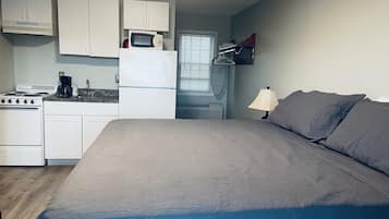 Habitación compacta con kitchenette, cama y ventana con persianas.