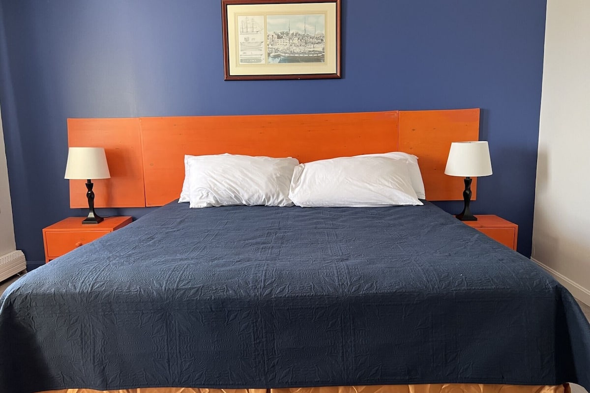 A neatly made bed with a blue and orange headboard, white pillows, and two bedside lamps.