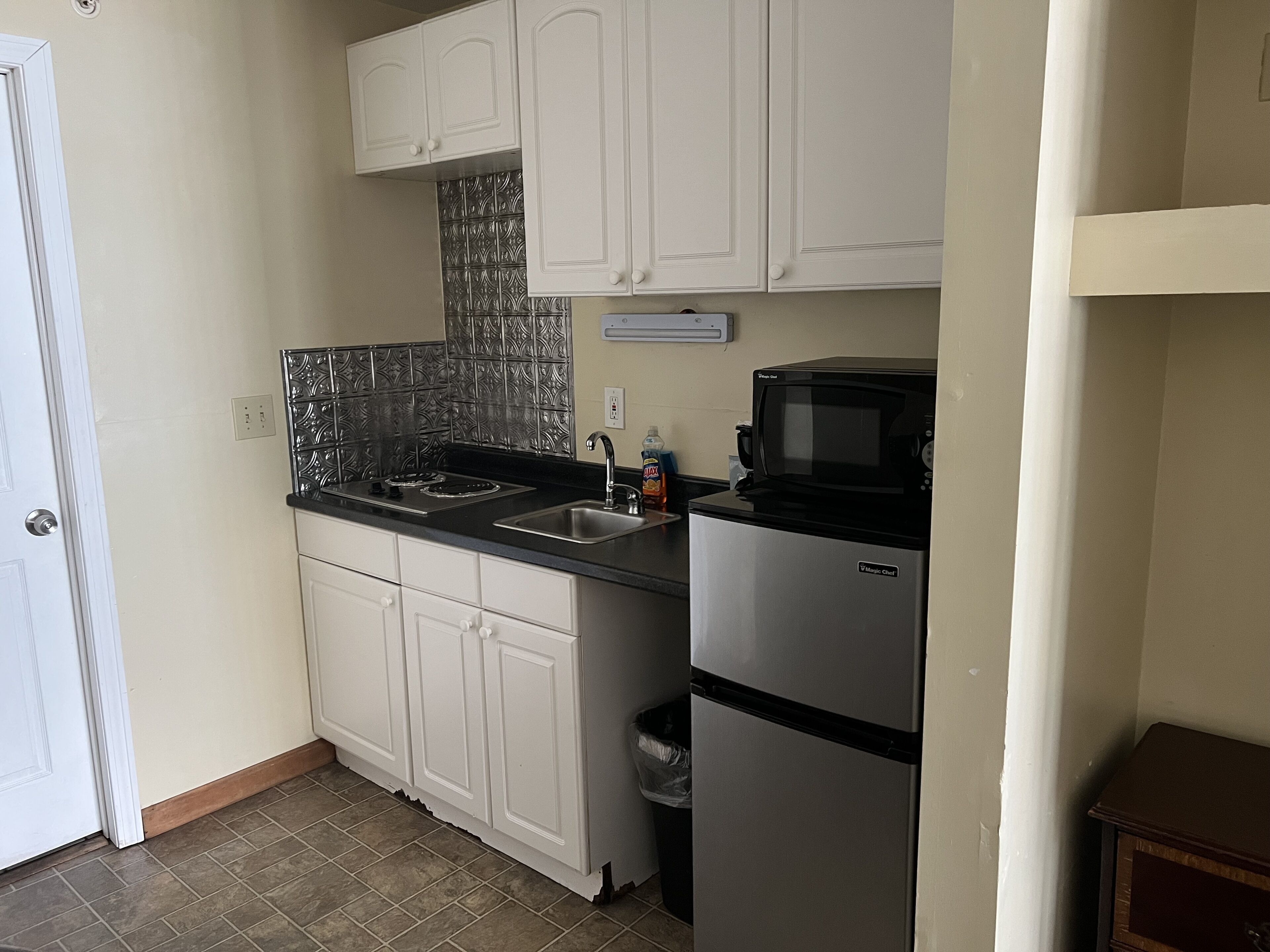 A small kitchen with white cabinets, a stainless steel refrigerator, a microwave, and a tiled backsplash.