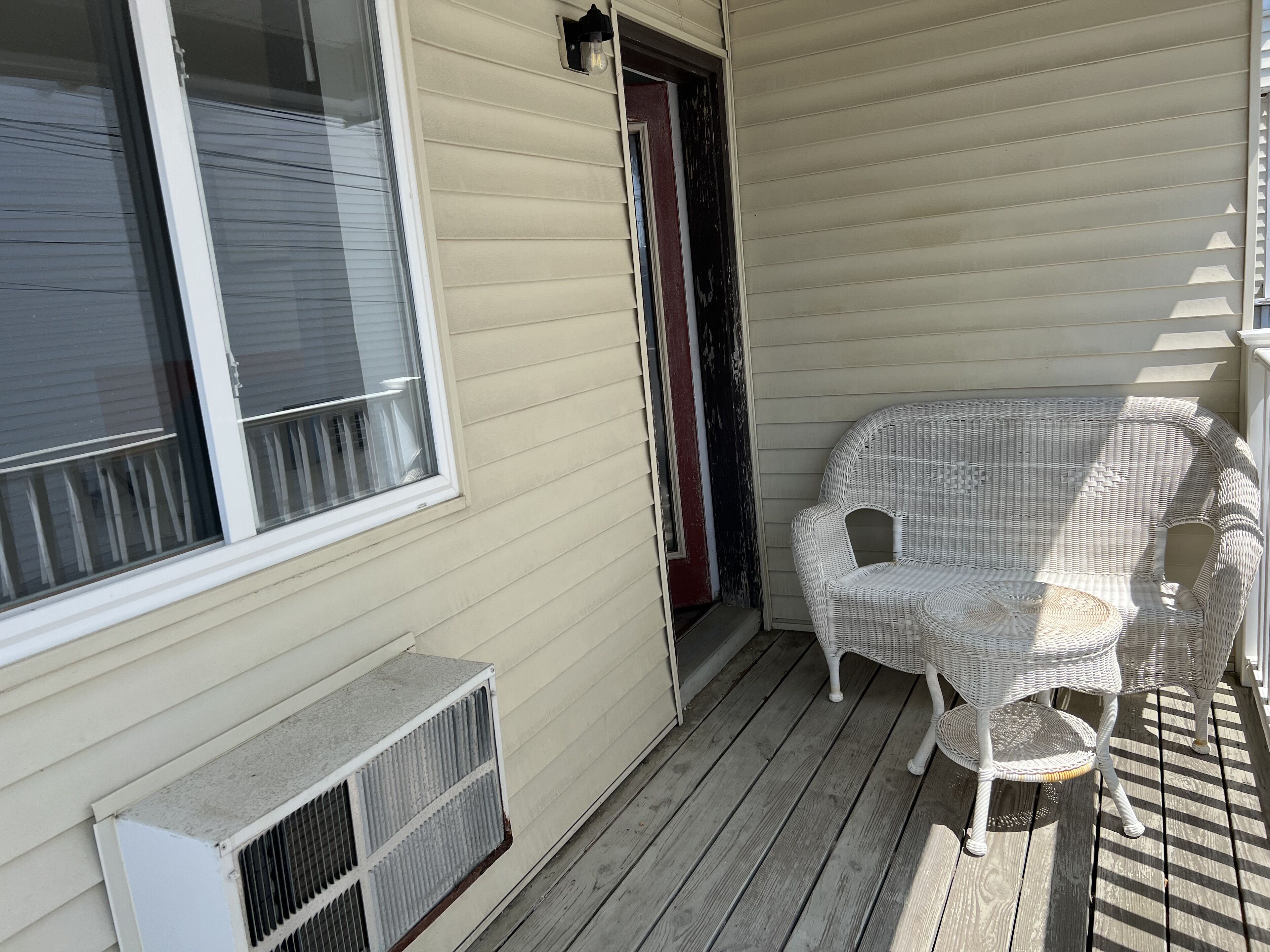 A porch with a wicker chair, a door, and a window.