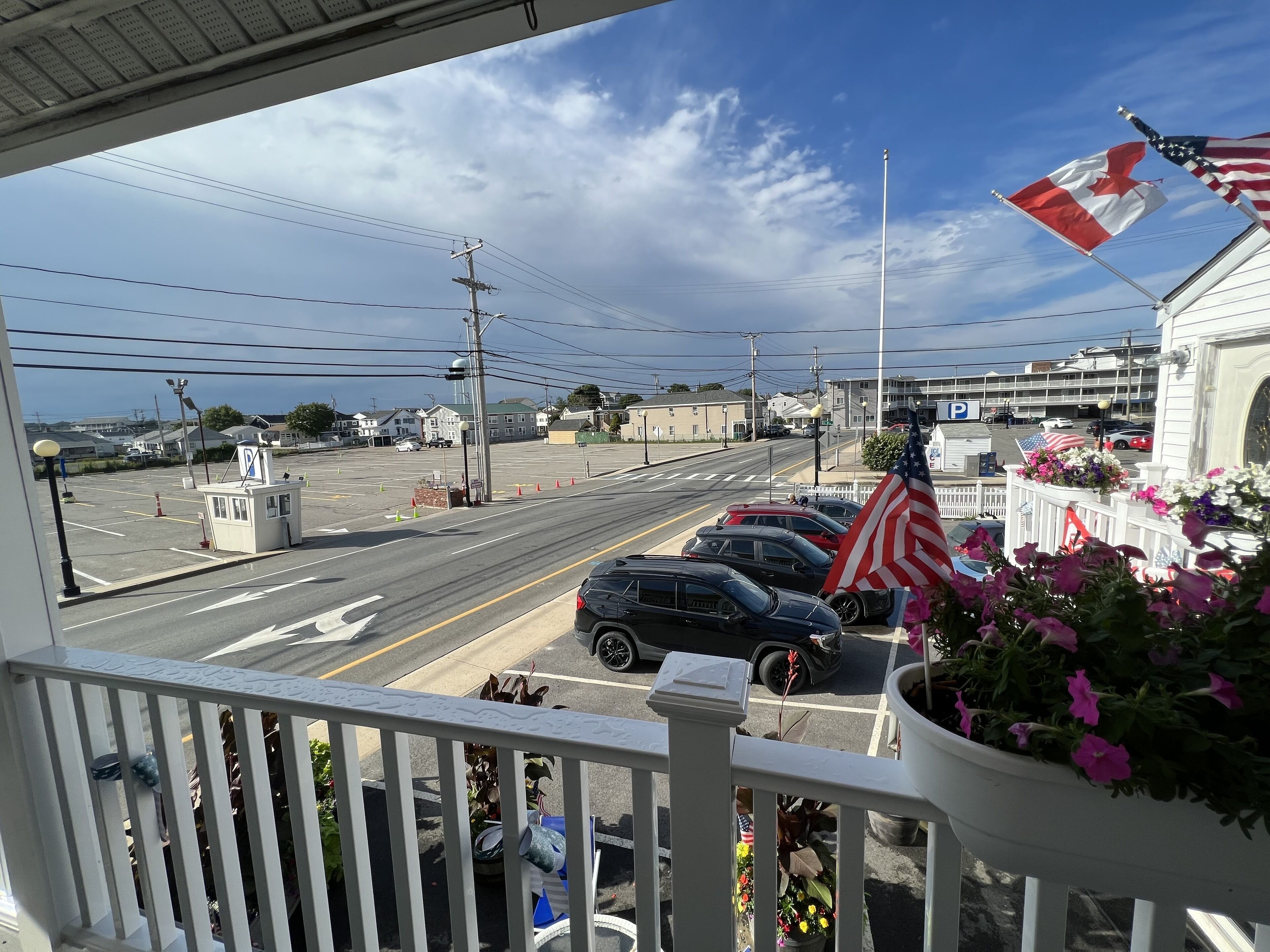 Une vue depuis un balcon donnant sur une rue où des voitures sont garées le long du trottoir, avec un feu de circulation et un bâtiment portant un panneau « P » indiquant un parking.