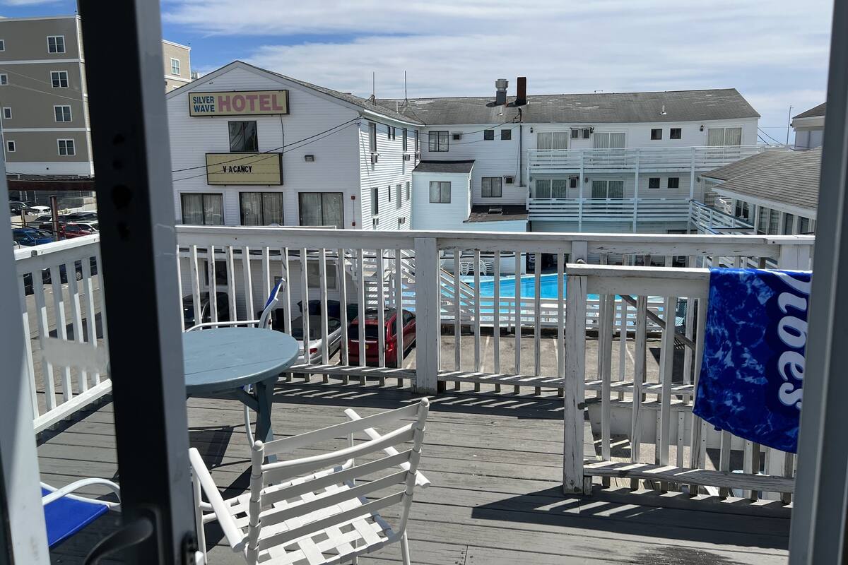 A hotel with a 'Vacancy' sign, a pool, and a wooden deck with chairs.