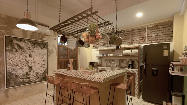 A kitchen with a central island, bar stools, hanging pots, and a refrigerator. - NEW Stylish Colonial House with Pool and Rooftop (Santa Marta)