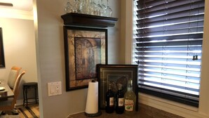 Un piano di lavoro in cucina con bottiglie di vino, una cornice con un'immagine e una finestra con persiane.