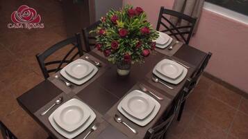 A beautifully set dining area with a centerpiece of roses, surrounded by four chairs and fine tableware.
