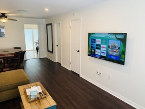 Uma sala de estar moderna com televisão de tela plana na parede, uma mesa de jantar de madeira, um sofá e uma mesa de centro.
