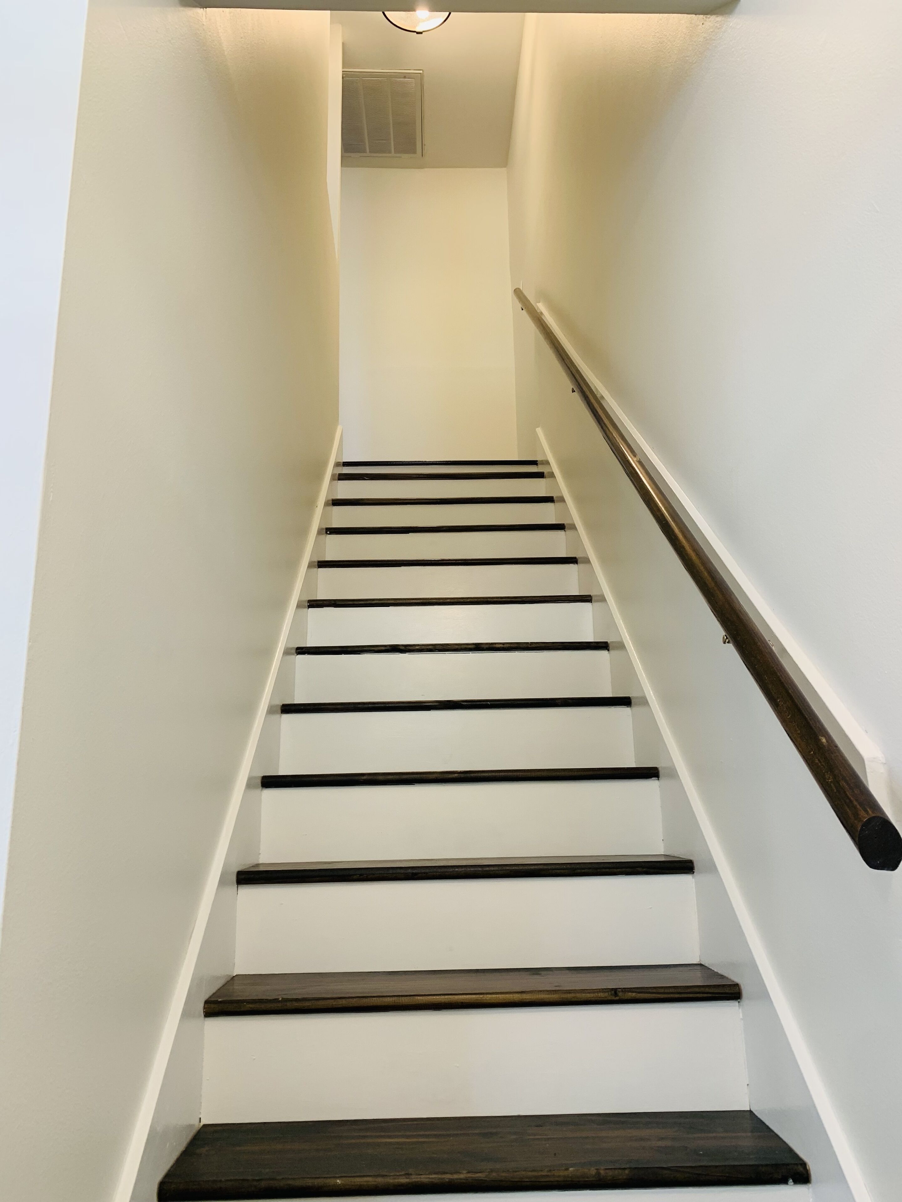 Una escalera estrecha de paredes blancas y escalones de madera oscura.