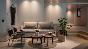 A modern living room with a sofa, two side tables, a coffee table, a chair, a potted plant, and a woven basket. - Made By The Sea Villa 5 (Malevizi)