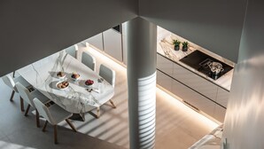 A modern dining area with a marble table and chairs, a kitchen with a sink and countertop, and a large pillar. - Made By The Sea Villa 5 (Malevizi)