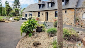 Une maison en pierre avec un toit en pente, une porte d’entrée et un petit porche agrémenté de plantes en pot.